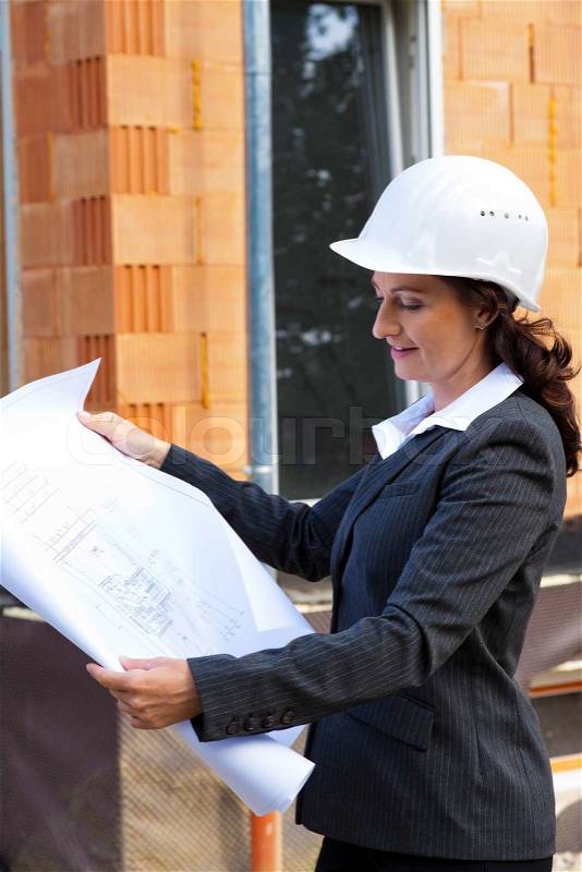 Architect with blueprint before shell of a house in house construction, stock photo
