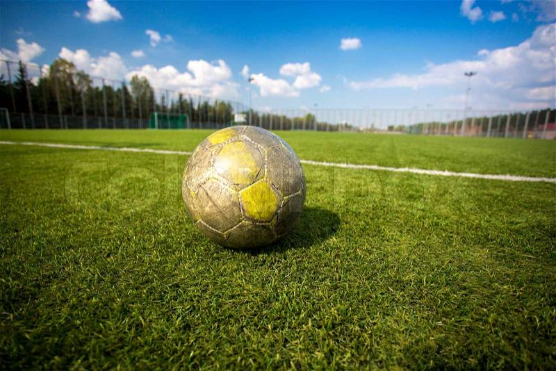 Old shabby soccer ball lying on artificial grass field, stock photo