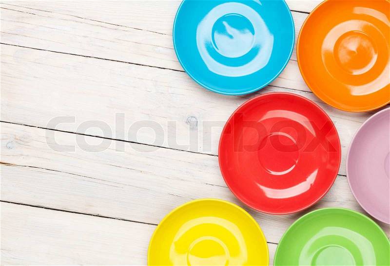 Colorful plates over white wooden table background with copy space, stock photo