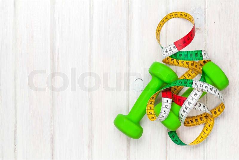Dumbells and tape measure over wooden background with copy space. Fitness and health, stock photo
