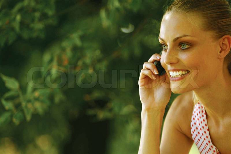 Young blond woman with mobile phone in the park , stock photo