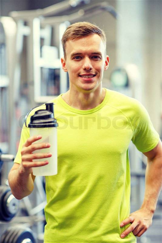 Sport, fitness, lifestyle and people concept - smiling man with protein shake bottle in gym, stock photo