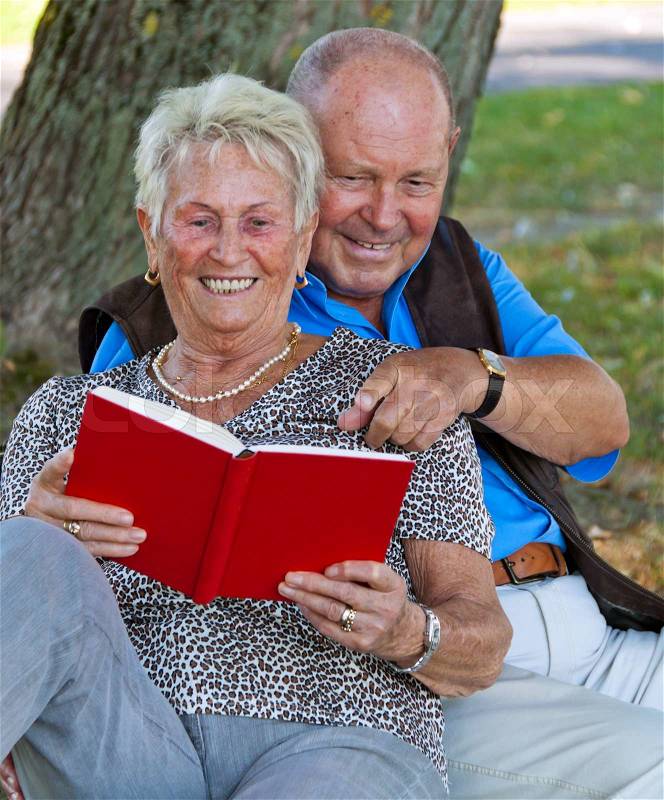 Mature couple in love senior citizens. Sitting in the park and read a book, stock photo