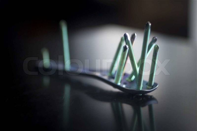Traumatology orthopedic surgery implant titanium plate and green screws in semi silhouette against plain studio background. Close-up macro photograph in grey tones. , stock photo
