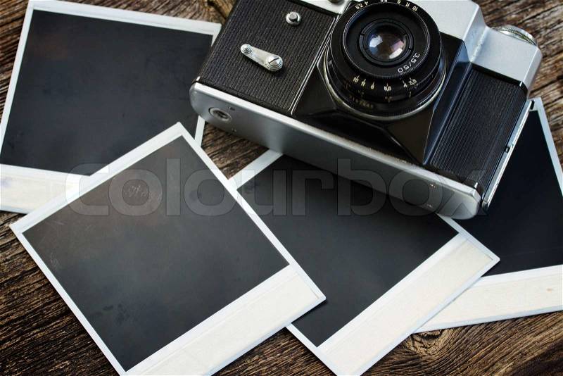 Vintage photo camera on pile of old instant photos on wooden table, stock photo