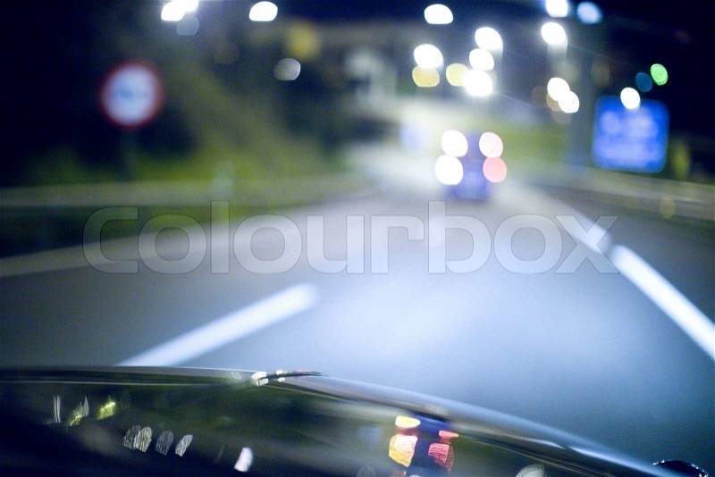 Road at night seen from inside car driving on motorway with highway and city lights in bokeh out of focus with shallow depth of focus on bonnet. , stock photo