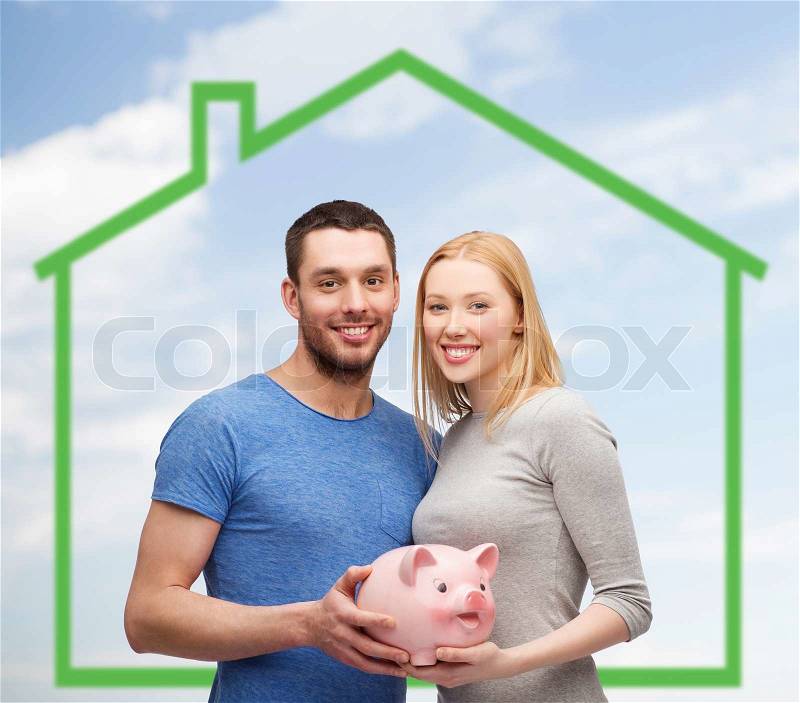 Love, home, people and family concept - smiling couple holding piggy bank over green house and blue sky with grass background, stock photo