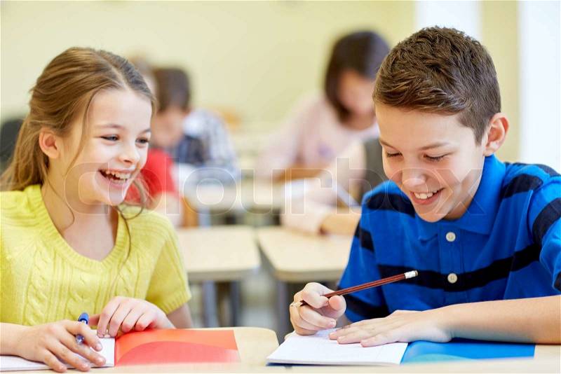Education, elementary school, learning and people concept - group of school kids with pens and notebooks writing test in classroom, stock photo