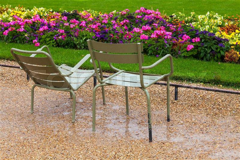 Wet metal armchairs in the rainy park with colorful flowers in Paris, stock photo