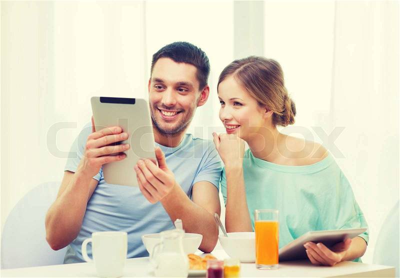 Food, home, couple and technology concept - smiling couple with tablet pc reading news and having breakfast at home, stock photo