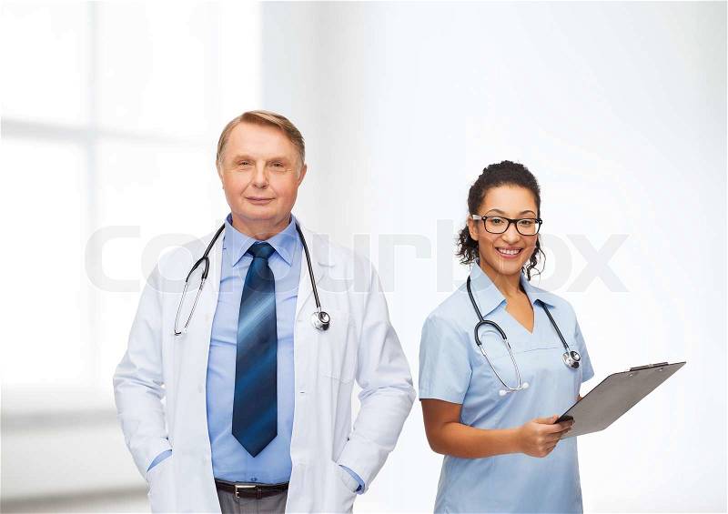 Healthcare, profession and medicine concept - smiling doctors with clipboard and stethoscopes over clinic background, stock photo