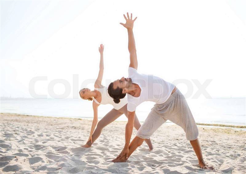 Fitness, sport, friendship and lifestyle concept - couple making yoga exercises on beach, stock photo
