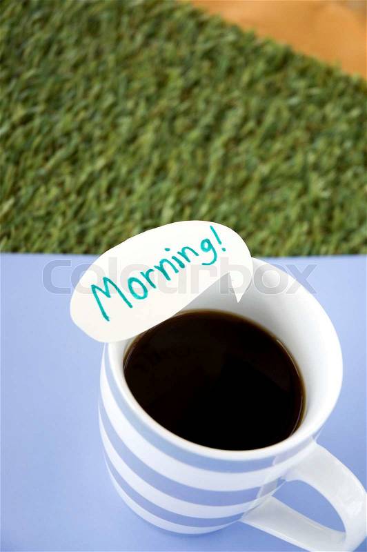 Morning note on coffee cup on blue and green grass background, stock photo