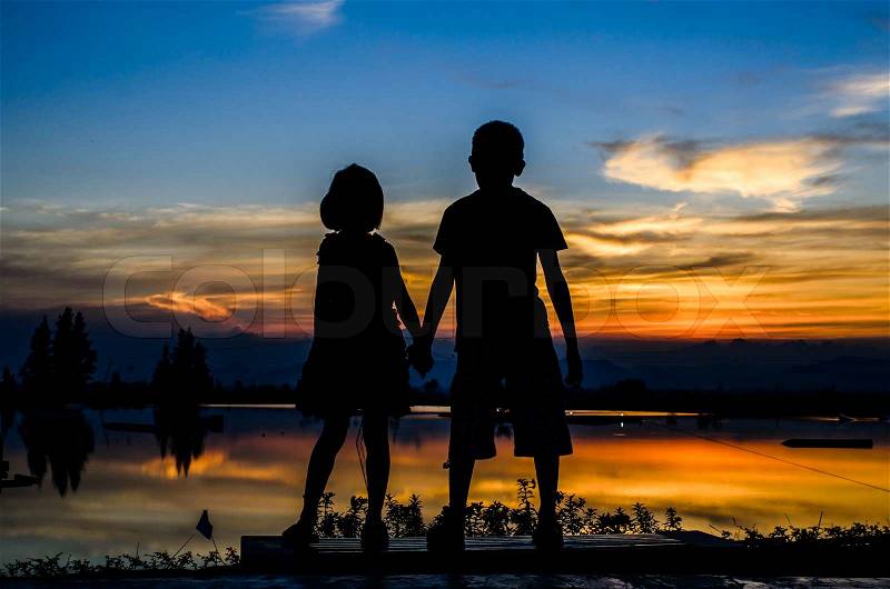 Brother and sister holding hands together with sun set, stock photo