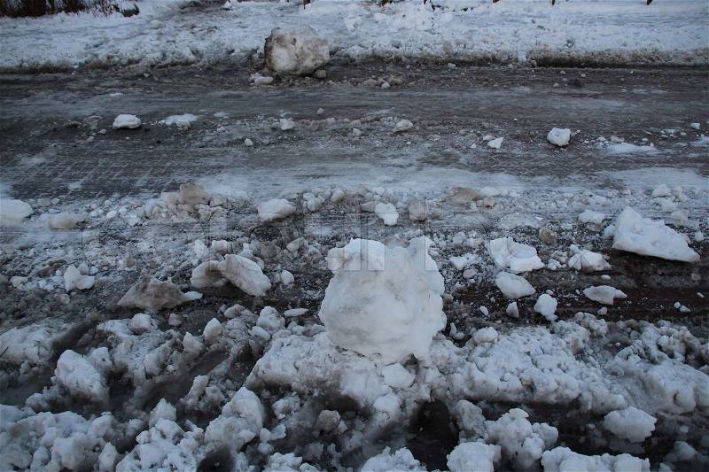 Traffic road is salted and a big snowball, prank, lies on the road in wintertime, stock photo