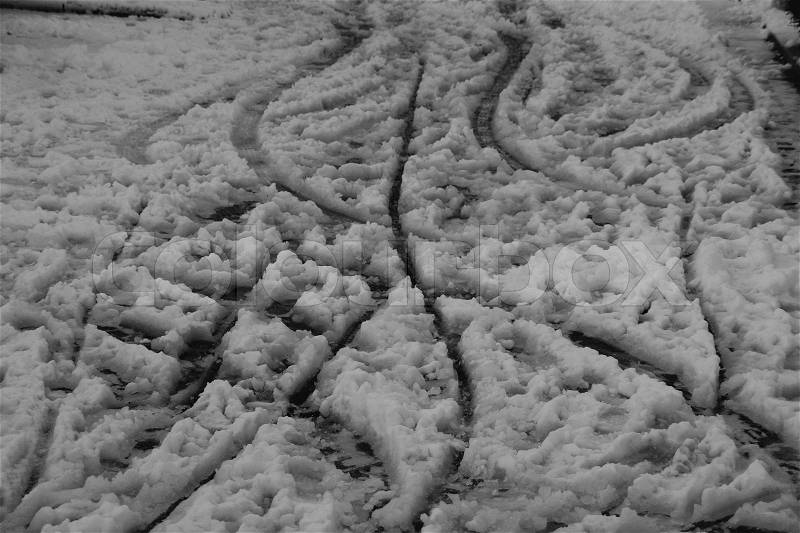 Be careful, freezing rain and snow on the footway with footprints and bike traces in the early morning in wintertime in black and white, stock photo