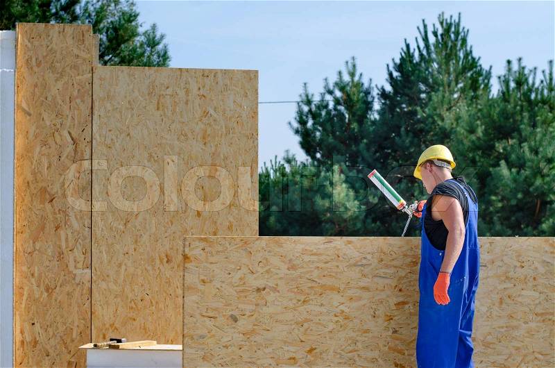 Builder applying glue to an insulated wooden wall panel on a building site for a new build house, stock photo