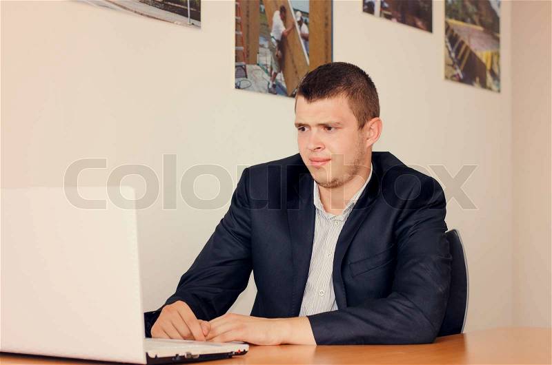 Young businessman with a concerned look reading the screen on his laptop computer leaning forwards to peer at the text, stock photo