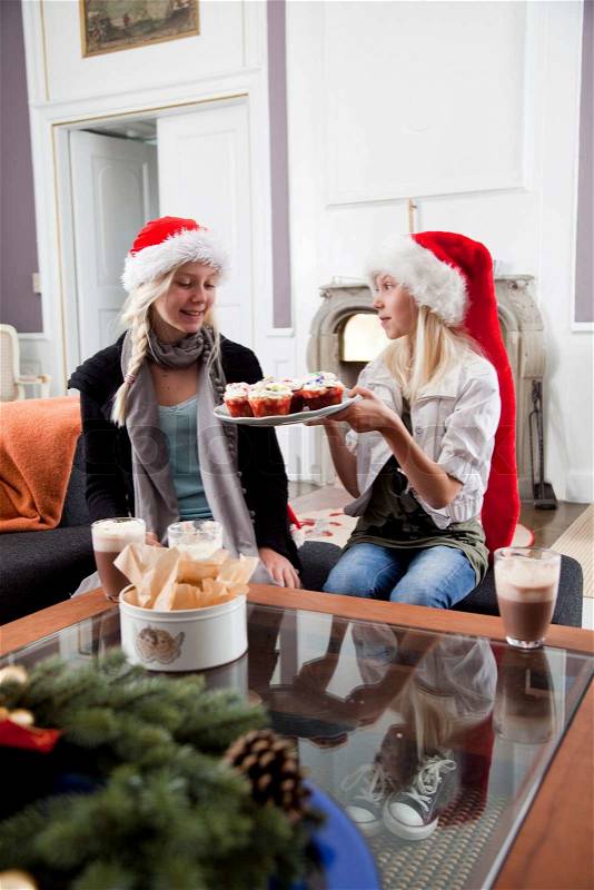 Two teenage girls with Santa hat eating muffins on Christmas day, stock photo