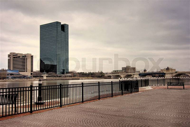A panoramic view of downtown Toledo Ohio\'s skyline from across the Maumee river at a popular restaurant area with a paver brick boardwalk and a decorative iron railing.. A stormy cloud filled sky for a backdrop, stock photo