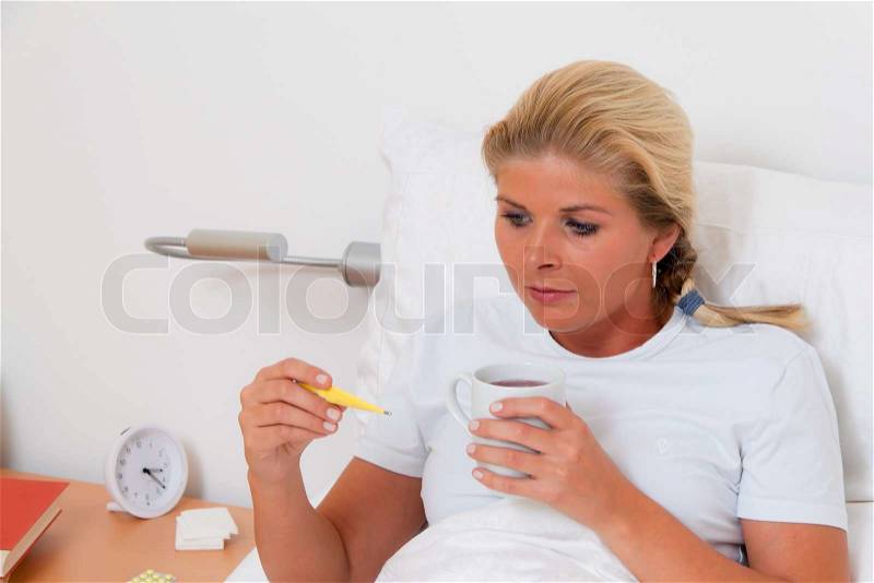 A woman is sick in bed and has a fever thermometer, stock photo