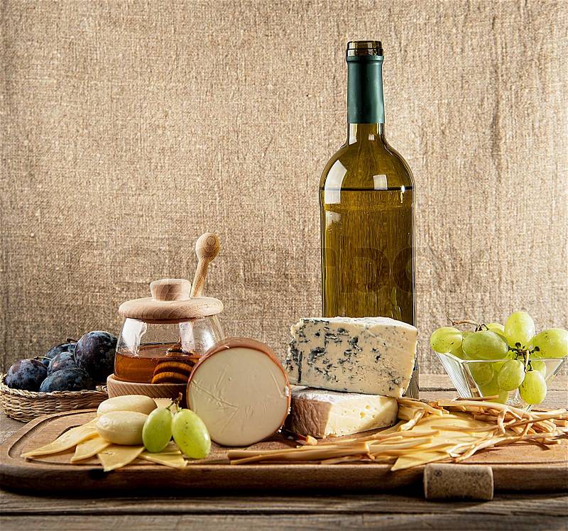 Various types of cheese, grapes, honey, wine bottle on the table, stock photo