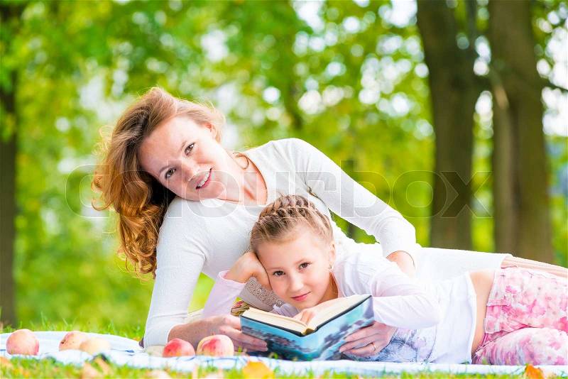 Mom and daughter reading a book lying in the park, stock photo