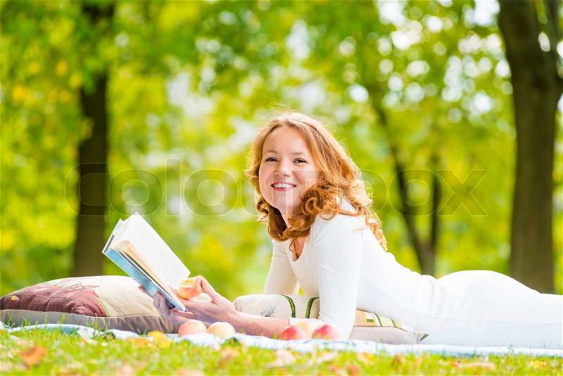 Laughing girl with a good book on the grass in the summer park, stock photo