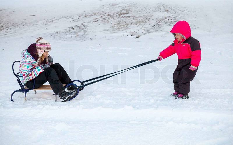 Little baby girl in pink pulling a sled on snowy winter road, stock photo