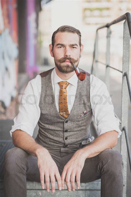 Handsome big moustache hipster man smoking pipe in the city, stock photo