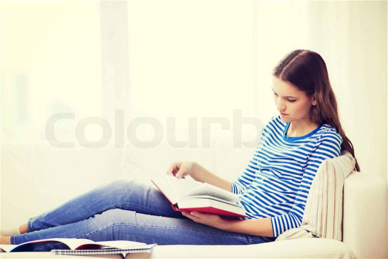 Leasure and home concept - calm teenage girl woman reading book and sitting on couch at home, stock photo