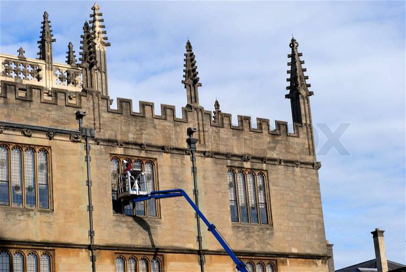 Window cleaner working high up on windows in collage building in Oxford, Oxfordshire, England, stock photo