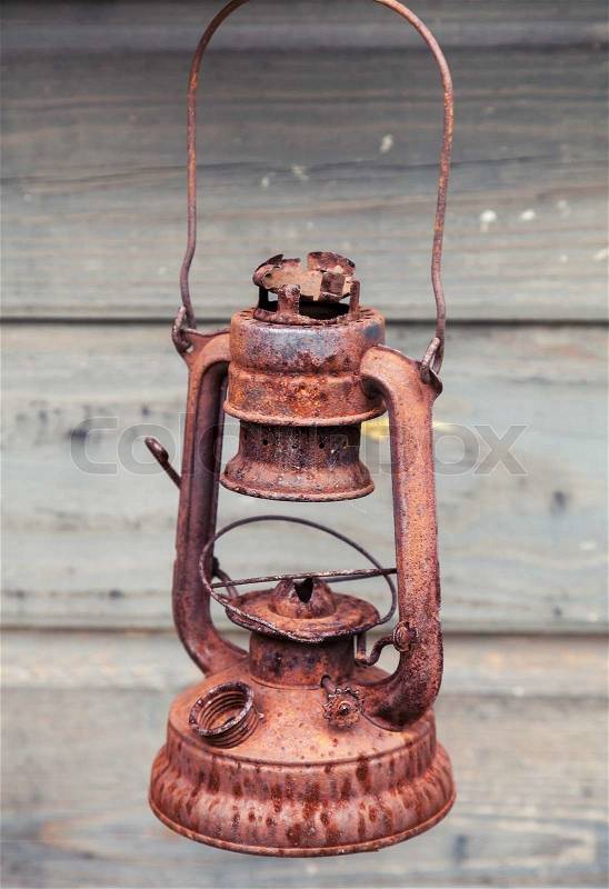Old rusted red kerosene lamp on gray wooden wall background, stock photo