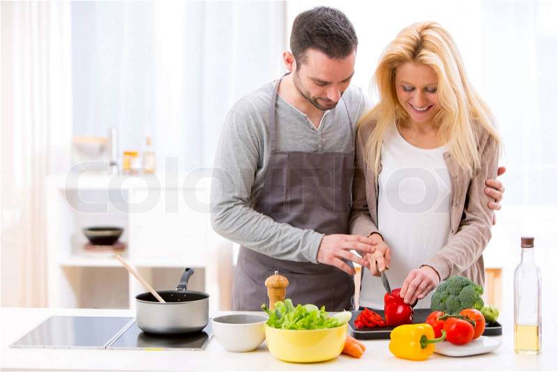 View of a Young attractive man helping out his wife while cooking , stock photo