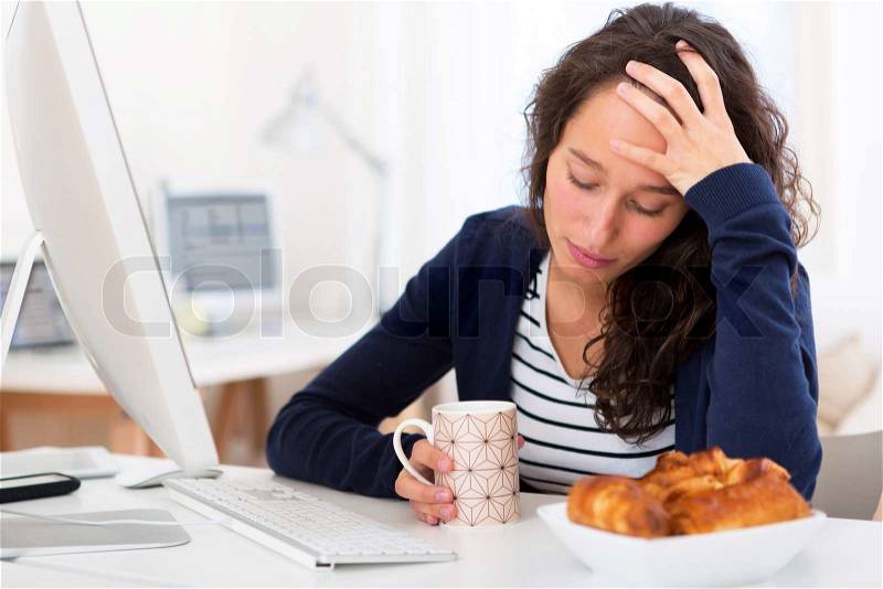 View of a Young tired student taking breakfast while working, stock photo