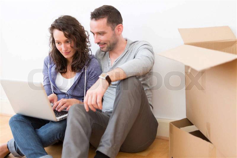 View of a Young couple using laptop while moving in new flat, stock photo