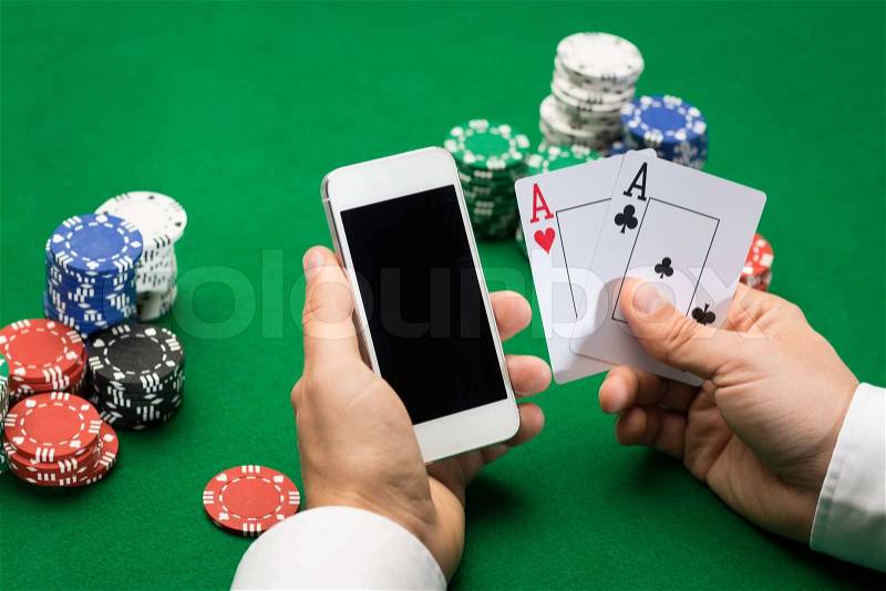 Casino, online gambling, technology and people concept - close up of poker player with playing cards, smartphone and chips at green casino table, stock photo