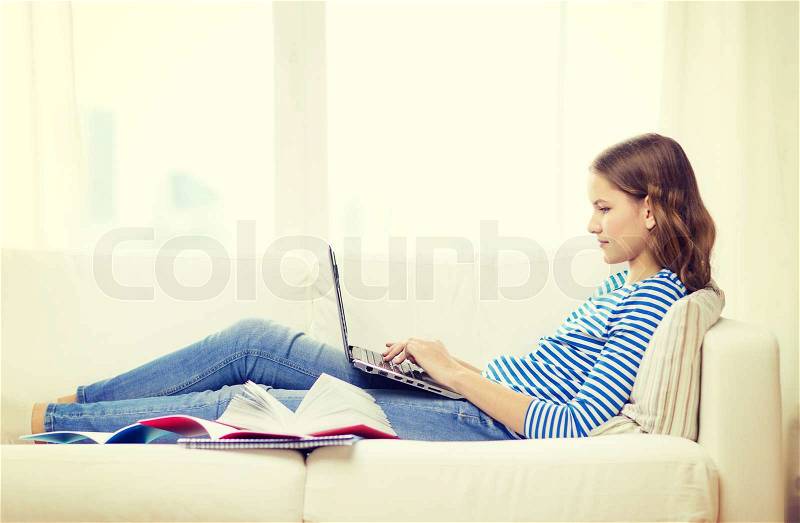 Home, technology and internet concept - busy teenage girl lying on the couch with laptop computer at home, stock photo