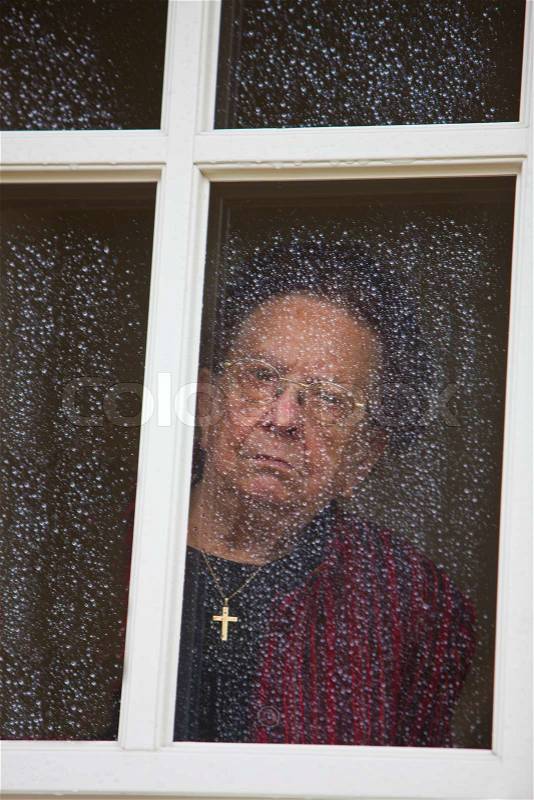 Old woman at the window with rain drops, stock photo