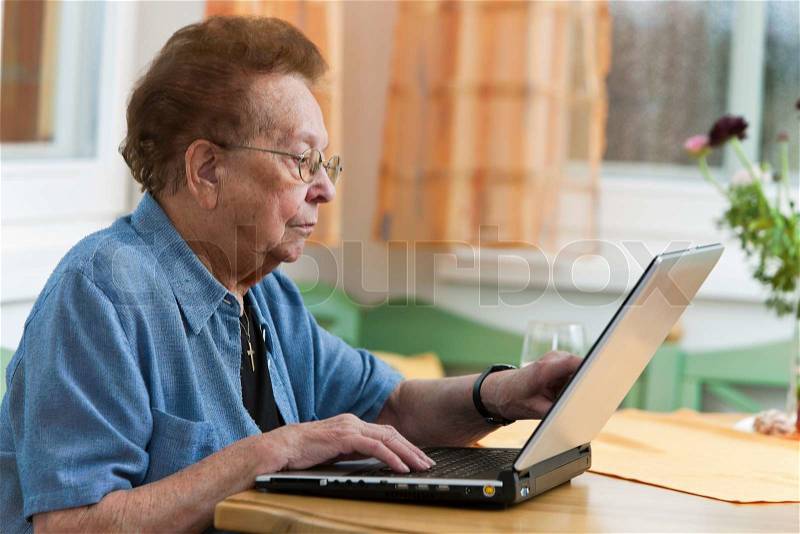 Old woman with a laptop writes e-mail, stock photo