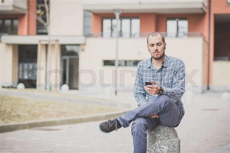 Handsome hipster casual multitasking modern man listening music and using smartphone in the city, stock photo