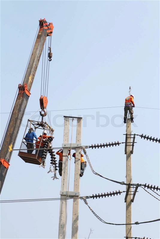 Electrician working at height by connect a high voltage wire, mobile crane lifting against the blue sky, stock photo