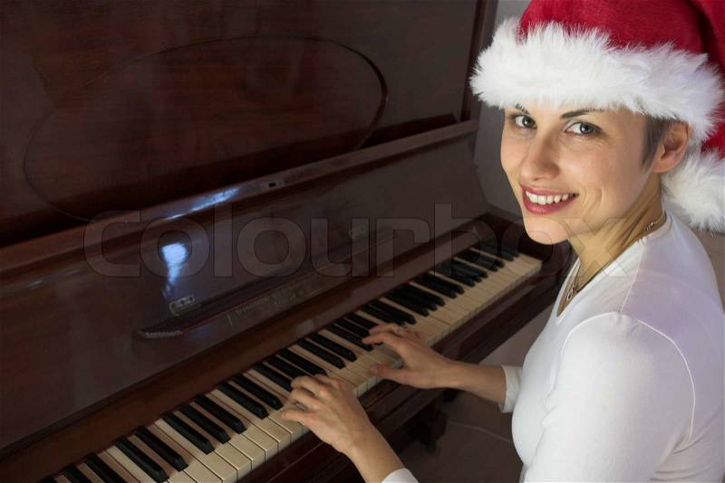 Blond short hair woman woman with white Tshirt playing piano with a santa hat, stock photo