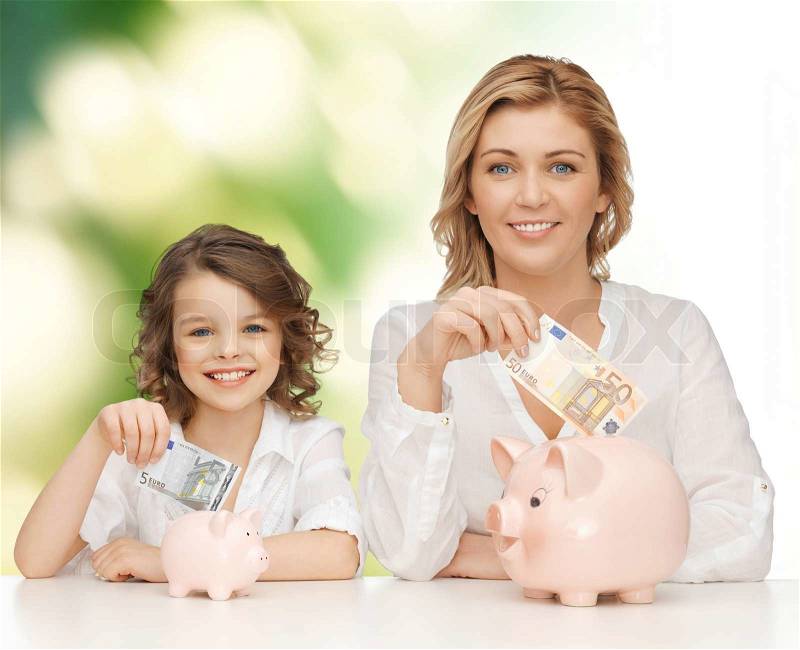People, finances, family budget and savings concept - happy mother and daughter with piggy banks and paper money over green background, stock photo