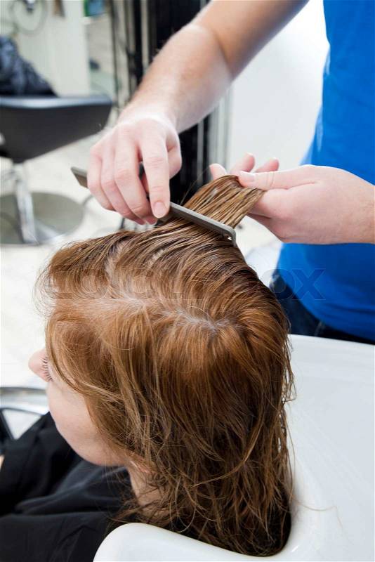 A hairstylist combing hair of a female costumer, stock photo