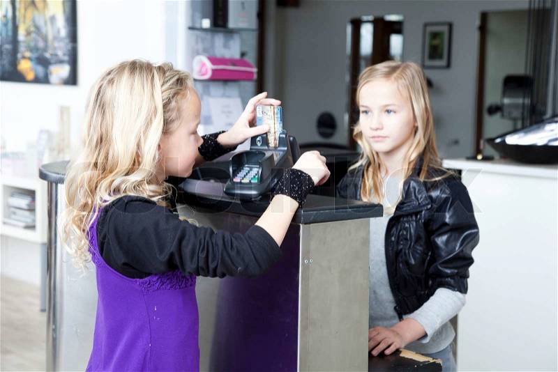 Two young girls in a beauty parlor using the credit card swiper, stock photo