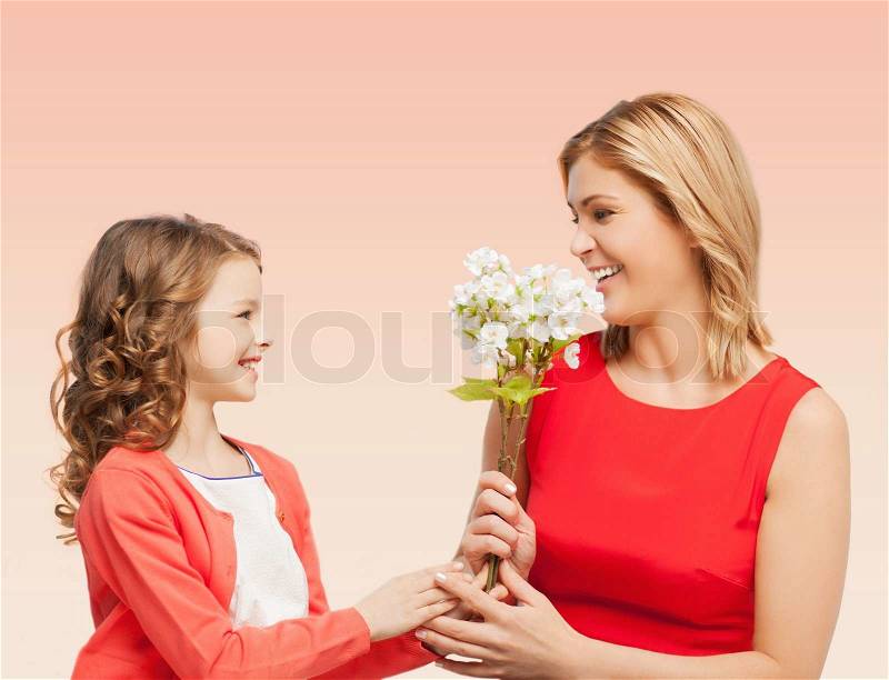 People, holidays, relations and family concept - happy little daughter giving flowers to her mother over beige background, stock photo