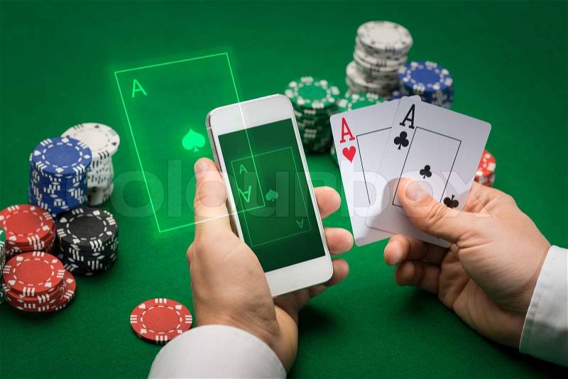 Casino, online gambling, technology and people concept - close up of poker player with playing cards, smartphone and chips at green casino table, stock photo