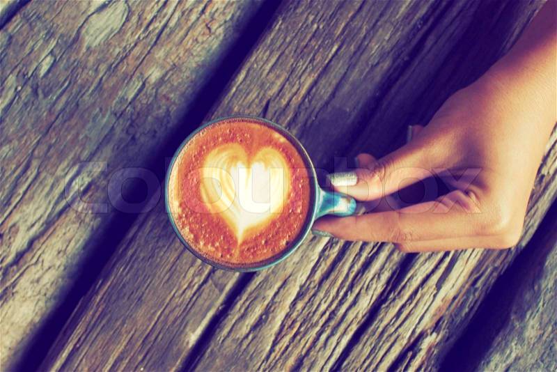 Hand and cup of coffee latte art on the wood background vintage color tone, stock photo