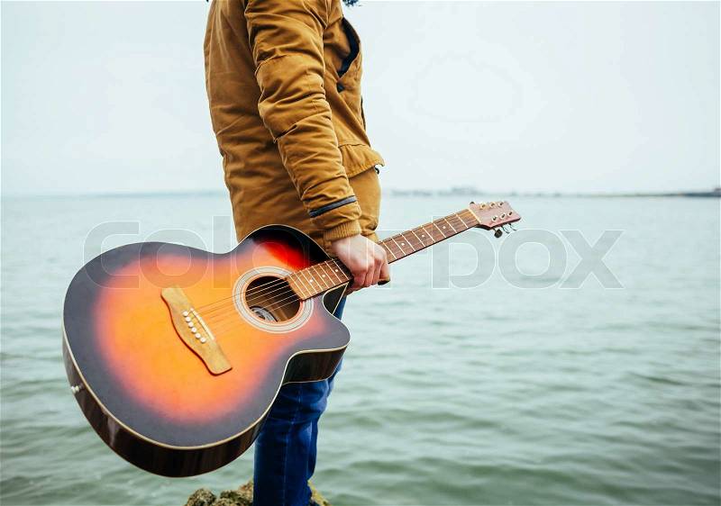 Young man holding guitar at the lake, stock photo